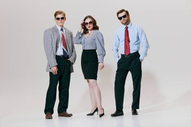 Üç şık profesyonel, beyaz stüdyo geçmişine karşı modaya uygun iş kıyafetleri içinde özgüvenli poz verdiler. Klasik şirket modasına modern bir dönüş. İş anlayışı, liderlik. Ad