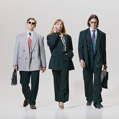 Bir kadın ve iki erkek, iş arkadaşları beyaz stüdyo geçmişine karşı büyük boy retro kıyafetler giyerek güvenle yürüyorlar. Şirket kültürü, iş ve tarz kavramı, liderlik. Ad