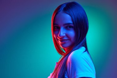 Çekici bir genç kızın kameraya şakacı bir şekilde bakması, neon ışıklarıyla gradyan stüdyonun arka planına karşı flört etmesi. İnsan duyguları, iş, güzellik ve moda kavramı, satış sezonu. Ad