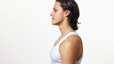 Beyaz arka planda bekleyen beyaz tişörtlü, duştan sonra ıslak saçlı esmer adamın yan görüntüsü. Doğal güzellik kavramı, moda, kozmetik ürünler, erkek sağlığı. Ad