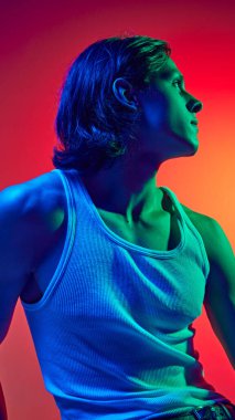 Mavi neon ışıklı portre. Uzun saçlı çekici bir adam. Stüdyonun arka planına karşı günlük kıyafetler giymiş. Doğal güzellik kavramı, moda, kozmetik ürünler, erkek sağlığı. Ad