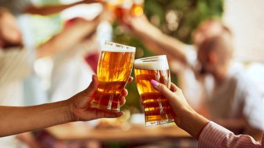 Spor taraftarları kadeh kaldırırken iki kadeh tokuştururken arka plandaki bulanık figürler neşe dolu tezahürat sahnesine derinlik katıyor. Ekim festivali, bira fabrikası, tatil, cuma havası. Reklam. Boşluğu kopyala.