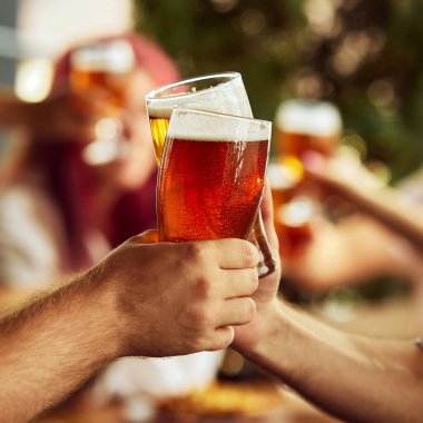 Spor hayranları arasında dinamik bir tost, bardaklar dolusu bira. Arka plan bulanıklığı paylaşılan heyecanı vurgular. Seçici odaklanma. Ekim festivali, bira fabrikası, tatil, cuma havası..