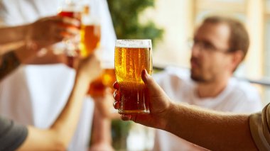Kahkahalar, şerefe ve bira bardakları havayı doldururken sporseverler oyunun heyecanını ve zafer yoldaşlığını kucaklıyor. Ekim festivali, bira fabrikası, tatil, cuma havası. Seçici odak.
