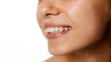 Ayrıntılı fotoğraf. Gülümsemenin yan profili, doğal dudaklara ve sağlıklı dişlere odaklanma, beyaz stüdyo geçmişine karşı güzellik ve yüz bakımının bir parçası. Güzellik, moda, görünüş, kişisel bakım kavramı.