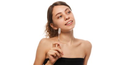 Elinde diş fırçası tutan gülümseyen kadın, beyaz stüdyo arka planına karşı günlük hijyen ve sağlığın önemini vurguladı. Güzellik, moda, görünüş, özgüven kavramı. Ad