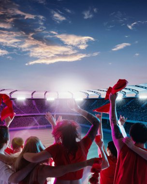 Kırmızı tişörtlü hayranlar renkli alacakaranlık gökyüzü altında bayrak ve eşarp sallayarak akşam güneşlenirken kutlama yapıyorlar. Spor eşitliği, şampiyonluk, kutlama, zafer kavramı. Ad