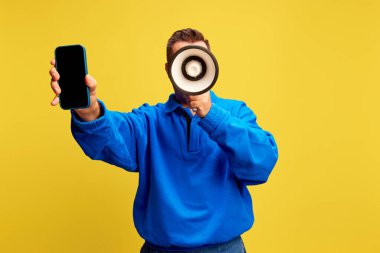 Man holds smartphone and megaphone, ready to announce latest mobile updates or services against yellow background. Concept of sale, shopping online, marketing, delivery service. Ad clipart