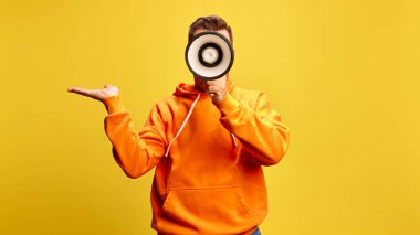 Adam megafona bağırıyor, omuz silkiyor ya da güneşli sarı arka plana karşı farkındalık yaratıyor. Kamu duyurusu, tartışma, iletişim, fikir. Ad.