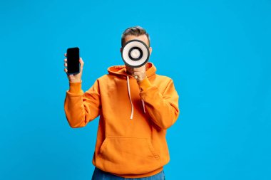 Man makes powerful statement with megaphone and smartphone in hand, bringing modern communication into focus. Concept of social media, delivery, online, modern marketing, promotions. clipart