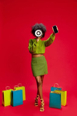 Woman in green sweater holds megaphone and smartphone, standing confidently with shopping bags on red background. Concept of marketing, retail, communication, online shopping, betting, clipart