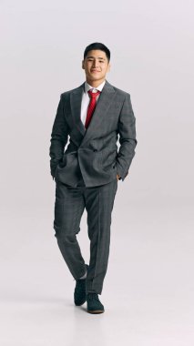 Resmi giyinmiş genç bir adamın beyaz stüdyo geçmişine karşı güvenle yürürken çekilmiş uzun bir fotoğrafı. Başarılı bir iş adamı. İş anlayışı, erkek modası, tarz, güzellik, estetik. Ad