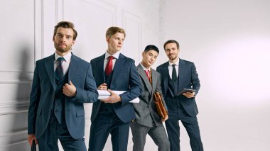 Ekip, beyaz stüdyo geçmişine karşı güven içinde poz veriyor. Her biri işle ilgili materyaller taşıyor ve bir sonraki iş girişimine hazır. Erkek modası, tarzı, güzelliği, estetiği. Ad