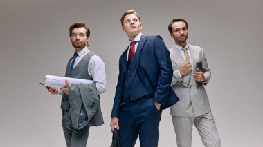 Birlikte çalışan bir grup adam, ellerinde iş eşyalarıyla. Dinamik ekip iş başında, beyaz stüdyo geçmişine karşı iş sorunlarını halletmeye hazır. Erkek modası, tarzı, güzelliği, estetiği. Ad