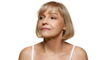 Beyaz stüdyo arka planına sakince bakan orta yaşlı, güzel bir kadının portresi. Uzayı kopyala Güzellik, sağlık, kozmetoloji, yaşlanmayı önleyici ürünler. Ad