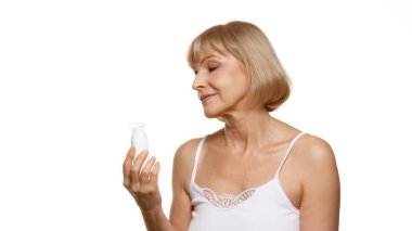 Cilt bakım ürünlerini sakin bakışlarla inceleyen güzel kadın, özbakım ritüellerini beyaz stüdyo geçmişine karşı kullanarak seçiyor. Güzellik, sağlık, kozmetoloji, yaşlanmayı önleme kavramı. Ad