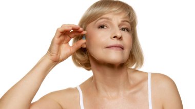 Beyaz stüdyo arka planında saç bakım kapsülü sunan orta yaşlı, güzel bir kadın. Spa tedavisi. Sağlıklı saçlar. Güzellik, sağlık, kozmetoloji, yaşlanmayı önleyici ürünler. Ad