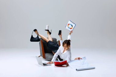 Görevin ortasında iş kadını, yerdeki kağıtları incelerken pano, telefon ve kahve fincanlarını dengeliyor. Baskı altında verimlilik. İş kavramı, çoklu görev, iş hayatı dengesi, verimlilik