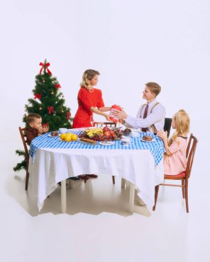 Noel masasında aile hediyelerini değiş tokuş eder. Verme ve alma heyecanı tatil atmosferine büyülü bir dokunuş katıyor. Noel konsepti, hediye değişimi, aile, şenlik neşesi, tatil.