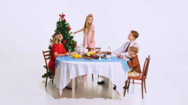 Küçük kız Noel ağacını aile yemeğinin tadını çıkarırken süslüyor. Sıcak ve bayram neşesi dolu festival sahnesine tatlı dokunuşlar getiriyor. Noel kavramı, dekorasyon, aile, bayram, şenlik.