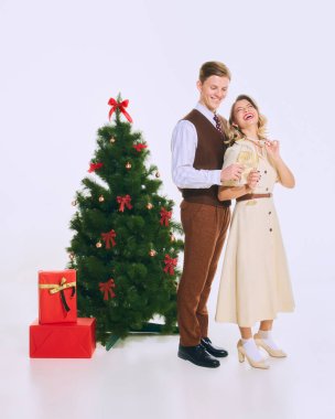 Çift Noel ağacının önünde neşeli pozlar veriyor, altında kırmızı hediyeler, şenlikli ve zarif bir atmosferde şampanya kadehleri tutuyorlar. Noel Kavramı, Neşe, Aile, Kutlama, Tatil