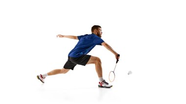 Badminton oyuncusu beyaz arka plana karşı vuruşunu mükemmel bir zamanlamayla ileri doğru hamle yapıyor. Yoğun konsantrasyon ve atletik hüner gösteriyor. Spor olayları kavramı, atletizm, odaklanma. AD
