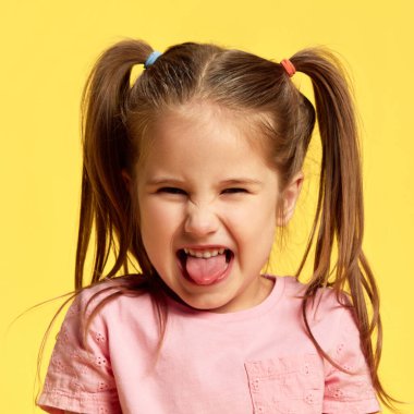 Küçük kızın güneşli sarı arka planda dilini dışarı çıkarırken yaramaz bir yüz ifadesi. Yüz ifadeleri, olumlu ve olumsuz duygular. Ad