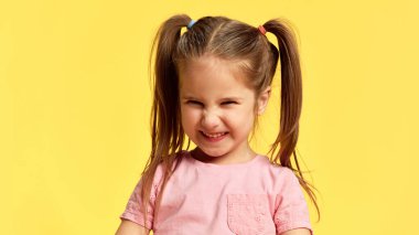 Kızın portresi gözlerini kapar, kıpır kıpır gülümser, saf neşeyle, güneşli sarı arka planda. Yüz ifadeleri, olumlu ve olumsuz duygular. Ad