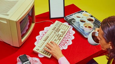 Yukarıdan bakıldığında, adamın kırmızı masada oturup kahve içerken yanında bir tepsi kahve fincanı ve eski PC klavyesiyle daktilo ettiği görülüyor. İş kavramı, iş hayatı dengesi. Pop sanat renkleri. Nostalji.