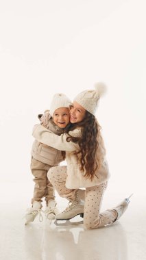 Ablası, buz üstünde dinlenirken küçük kardeşini rahatlatıyor. Beyaz stüdyo arka planına karşı eğlencenin ortasında sessiz bir kardeş anı. Kış zamanı kavramı, yeni yıl tatili, Noel tatili. Ad