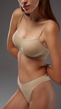 Bej iç çamaşırlı manken kendine güvenen pozlar sergiliyor, vücudunun üst kısımlarına odaklanıyor ve sıcak gri arka plana karşı duruşunu sergiliyor. Kadın sağlığı diyeti kavramı, doğal güzellik, sağlık. Ad