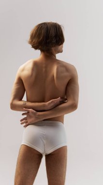 Sağlıklı sırtlı genç bir adamın, gri stüdyo arka planına karşı tanımlanmış kaslarını sergilemesi. Doğal güzellik kavramı, erkek sağlığı, moda, cilt bakımı. Ad