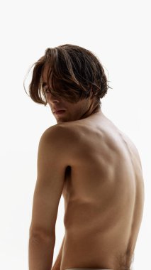 Üstsüz poz veren genç bir adamın portresi ve beyaz stüdyo arka planına karşı omuz omuza kameraya bakmak. Erkek model çıplak sırtını gösteriyor. Doğal güzellik kavramı, erkek sağlığı, moda. Ad
