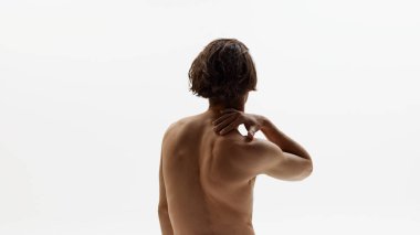 Üstsüz, genç, atletik erkek modelin arka planı elini nazikçe beyaz stüdyo arka planına koydu. Sağlıklı ve kaslı. Doğal güzellik kavramı, erkek sağlığı, moda, cilt bakımı. Ad