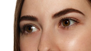 Açık kahverengi gözlü, uzun kirpikli ve beyaz arka planda pürüzsüz ciltli genç bir kadının yakın plan fotoğrafı. Güzellik, sağlık, tazelik, sağlık, güven kavramı. Ad