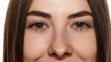 Açık kahverengi gözlü, uzun kirpikli ve beyaz arka planda pürüzsüz ciltli genç bir kadının yakın plan fotoğrafı. Güzellik, sağlık, tazelik, sağlık, güven kavramı. Ad