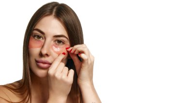 Çıplak omuzlu bir kadın, beyaz arka planda hidrasyon için göz altı hidrojel bantları uyguluyor. Kopyalama alanı olan. Güzellik, sağlık, tazelik, sağlık, güven kavramı. Ad