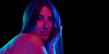 Sakin bir ifadeyle genç bir kadının portresi, eline yaslanmış ve parlak neon ışıkta siyah stüdyo arka planına doğru kameraya bakıyor. Güzellik kavramı, kendine bakım, kozmetoloji tedavisi. Ad