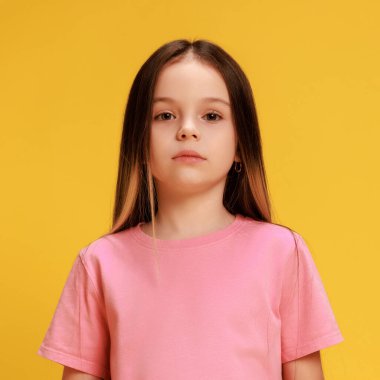 Sakin küçük bir kızın portresi, sarı stüdyo arka planına güvenle bakan bir öğrenci. Sıradan giyinmiş bir çocuk. Çocukluk kavramı, yaşam tarzı, ifadeler, moda. Ad