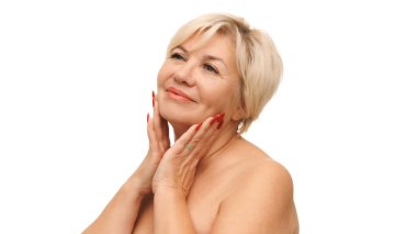 Beyaz stüdyo arka planında yumuşak ve pürüzsüz tenine dokunan 60 'lı yaşlardaki güzel beyaz kadın. Doğal güzellik kavramı, spa tedavisi, kozmetoloji.