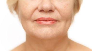 Cropped photo of mature female lips with lipstick against white studio background. Plump, moisturized lips. Mimicable wrinkles. Concept of natural beauty, spa treatment, cosmetology.