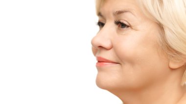Parlak cildi olan olgun bir kadın, ince makyajı beyaz stüdyo geçmişine karşı doğal özelliklerini geliştiriyor. Doğal güzellik kavramı, spa tedavisi, kozmetoloji, yaşlanma karşıtı prosedürler.