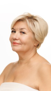 Nazik gülüşü ve ışığı olan olgun bir kadının portresi beyaz stüdyo arka planında poz veriyor. Cilt bakımı rutini. Doğal güzellik kavramı, spa tedavisi, kozmetoloji.