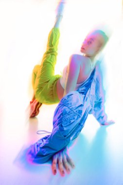 Çağdaş sanat kolajı. Dinamik bir şekilde yere uzanan, parlak neon ışık efektleriyle çevrili canlı atletik giysiler giyen bir kadın. Moda, tarz, yaşam tarzı kavramı. Hareket bulanıklığı etkisi.