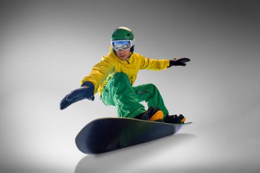 Genç atletik adam modern, parlak sarı ve yeşil takım elbiseli gri stüdyo geçmişine karşı numaralar yapmaya hazır. Düşük açı. Ekstrem spor, enerji, hız, moda kavramı.