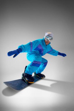 Grevdeki kar kaykaycısı, gri stüdyo arka planına karşı, ekstrem sporlar ve maceranın heyecanını somutlaştıran numaralar yapıyor. Ekstrem spor, enerji, hız, moda kavramı.