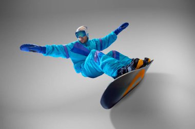 Snowboardcu, gri stüdyo arka planına karşı harekete geçmek için eski mavi tulum giymişti. Kış sporlarında klasik tarzın cazibesini yakalıyordu. Ekstrem spor, enerji, hız, moda kavramı.