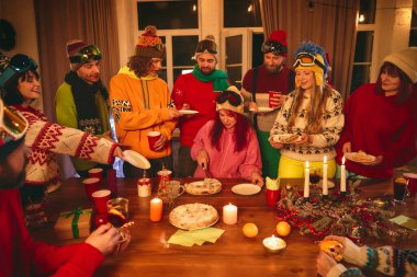 Kayak temalı kış kıyafetleri giymiş arkadaşlarla mum, taze meyve ve hamur işi dolu ahşap masanın etrafında kutlama sahnesi. Tatil kavramı, Noel partisi. Ad