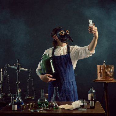 Elinde büyük cam kavanoz tutan veba maskeli adam modern selfie çekerek alışılmadık demleme ve damıtma çalışmalarını ima ediyor. Dönem, tıp, bilim ve ilaç karşılaştırmaları kavramı.