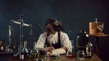 Veba maskeli gizemli adam klasik laboratuvar ekipmanlarının arasında oturuyor ve esrarengiz geçmişine karşı klasik laboratuvar tüyleriyle not alıyor. Tıp, bilim, ilaç kavramı..